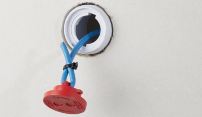 Blue electrical wires with a red protective cap extend from a circular white junction box opening in a clean white wall